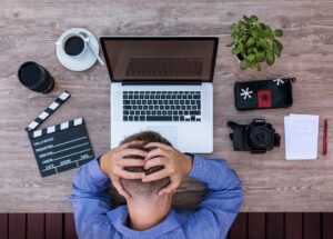 Man holding his head over his laptop with a headache